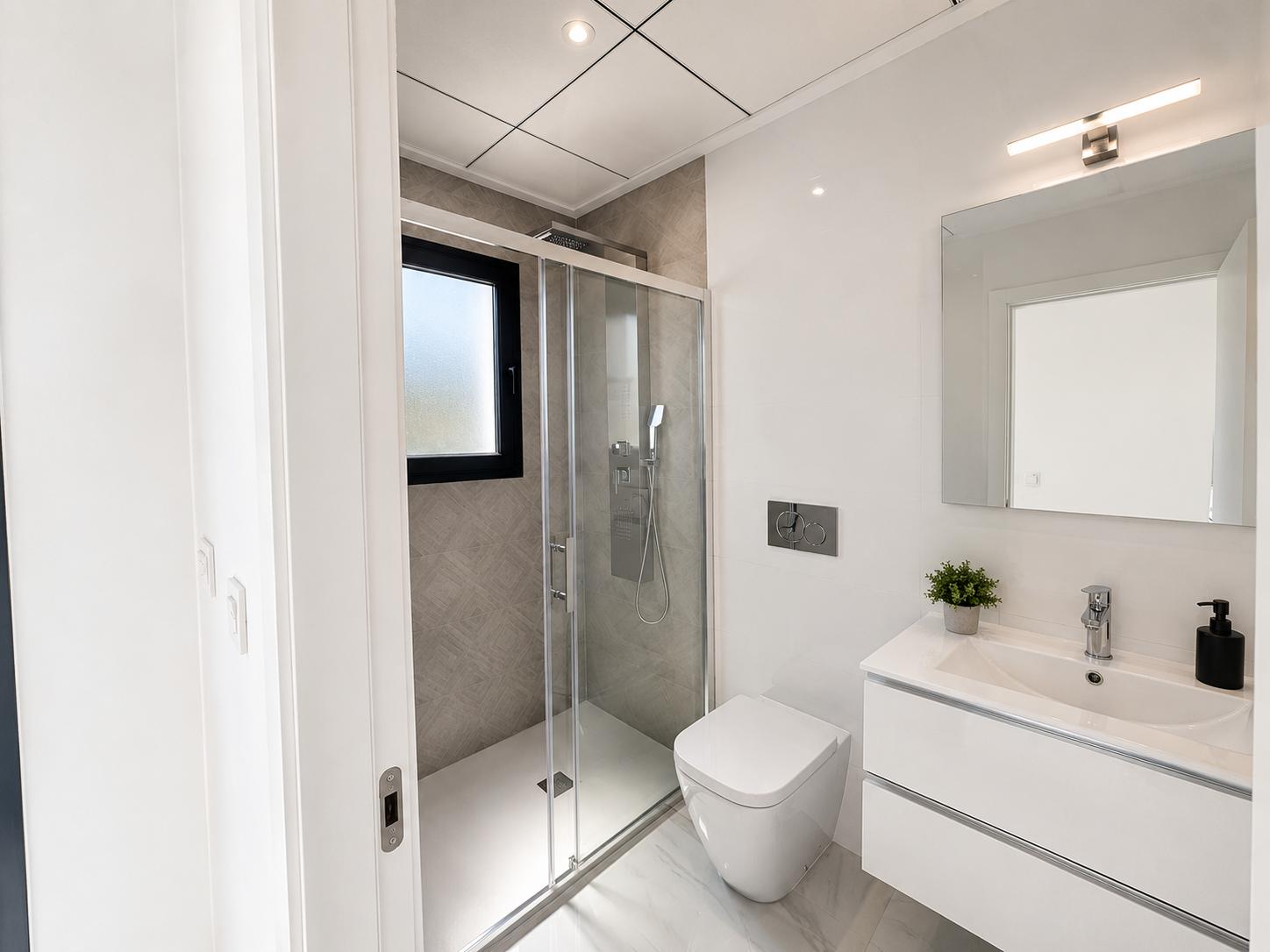 Modern bathroom featuring a floating white vanity, wall-mounted toilet, and a walk-in shower with textured grey tiles and a frosted window. Marble-effect floor tiles complete the sleek design.