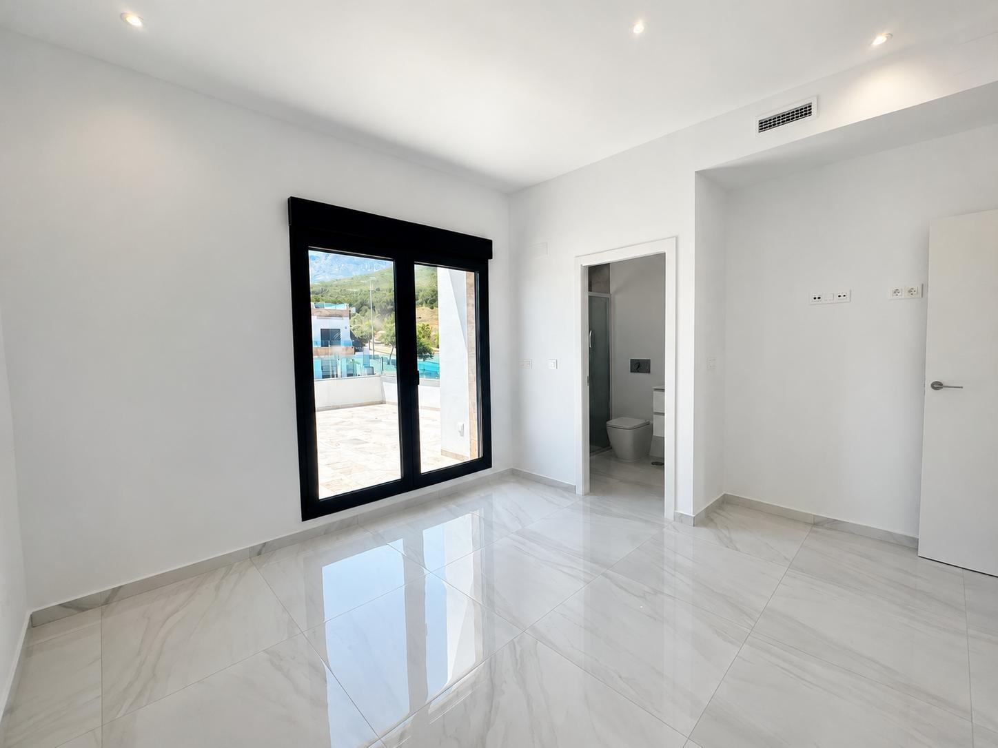 Spacious bedroom featuring glossy porcelain tile flooring, direct terrace access, and an en-suite bathroom. Recessed lighting and ducted air conditioning vent are visible.