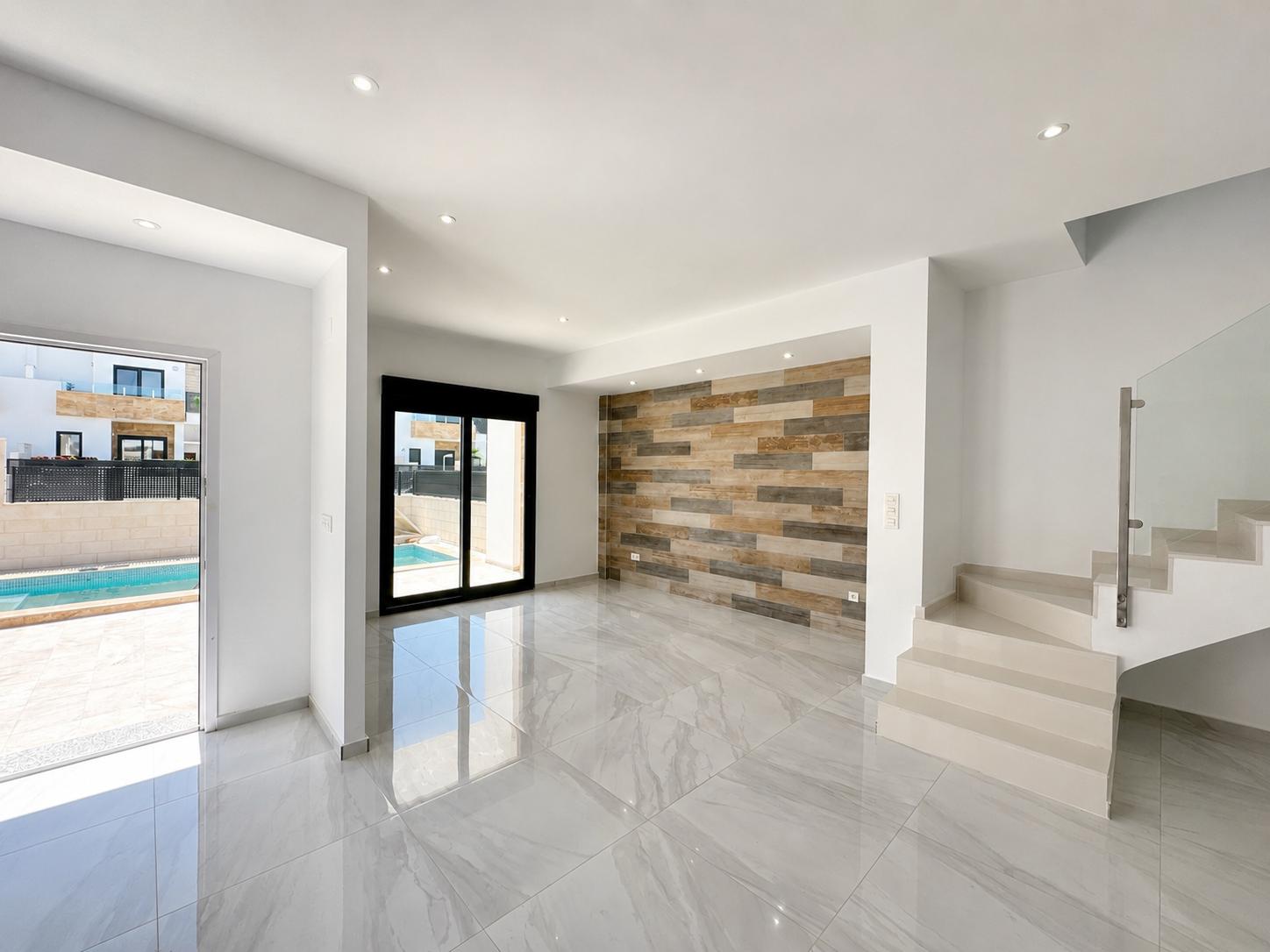 Spacious living area featuring polished porcelain tiles, a decorative wood-effect panel wall, and direct access to the private pool. Modern staircase with glass railing.