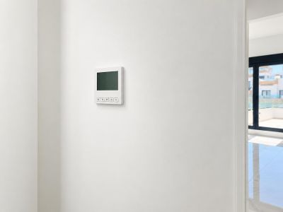 A sleek digital climate control panel is mounted on a pristine white wall, offering a glimpse into a bright adjacent room with tiled flooring and an outdoor terrace view.