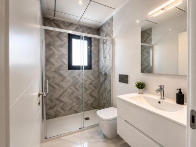 Contemporary bathroom featuring a walk-in shower with glass screen, grey geometric wall tiles, and a window. White floating vanity above marble-look flooring.