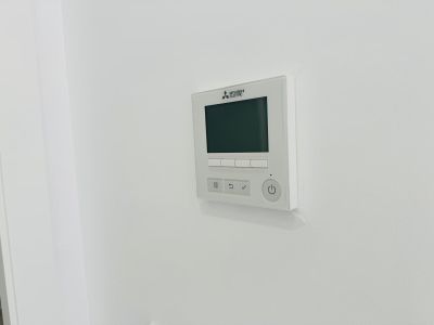 Mitsubishi Electric control panel for ducted air conditioning, featuring a digital display and intuitive buttons, integrated seamlessly into the white wall.