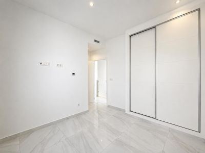 Modern room featuring large white built-in sliding wardrobes, light grey marble-effect floor tiles, and recessed ceiling lights. A clean, functional design.