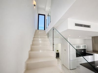 Modern staircase with light-toned steps and a sleek glass railing, leading to an exterior door. A contemporary kitchen with black countertops and a partial view of a bathroom are visible.