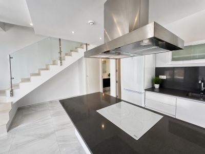 Open-plan kitchen featuring a dark countertop island with a white induction hob, adjacent to a modern staircase with glass balustrade and white steps.