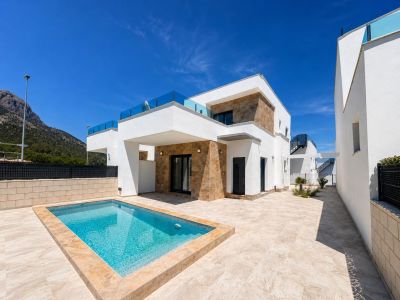 The modern villa exterior showcases a rectangular private pool and an expansive light-tiled terrace. White facades with natural stone accents and glass balustrades frame clear mountain views.