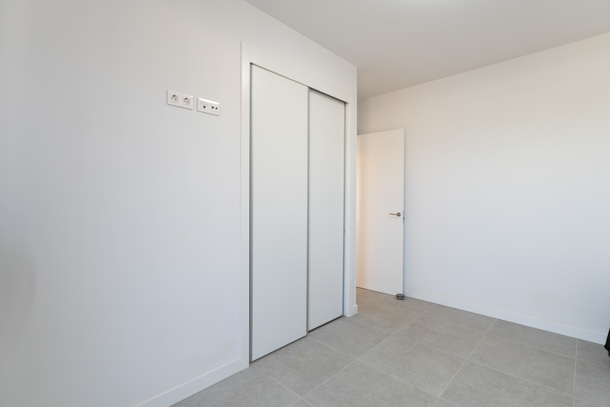Bedroom featuring a spacious built-in wardrobe with white sliding doors and light grey tiled flooring. Modern electrical and data outlets are visible.
