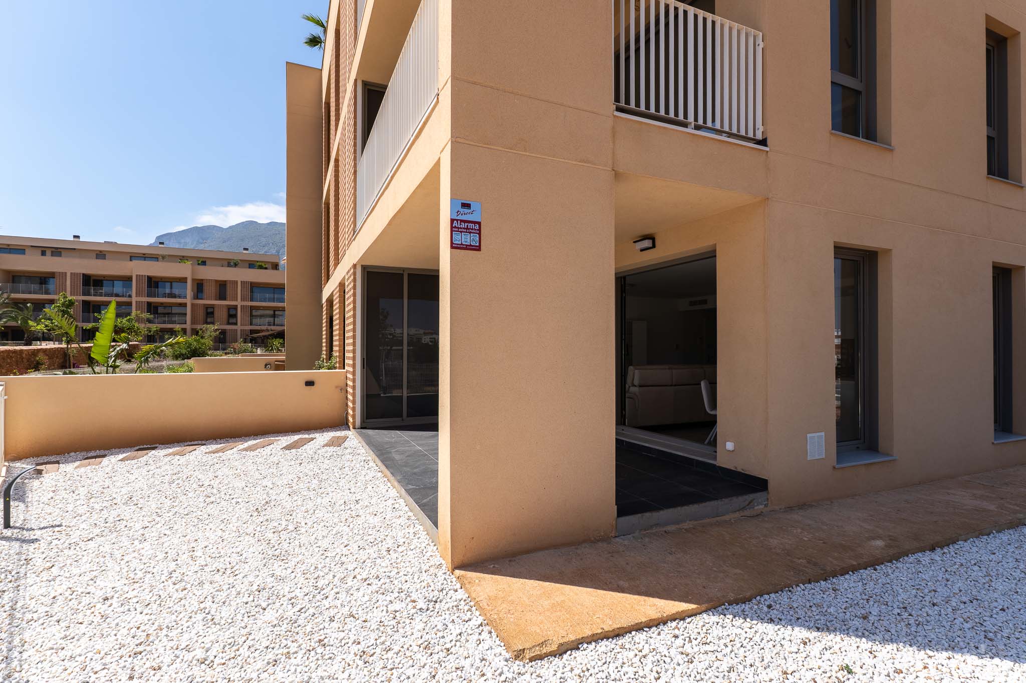 Ground floor exterior featuring a modern ochre facade. Includes a private white gravel garden and a covered terrace with direct access to the interior, offering mountain views.