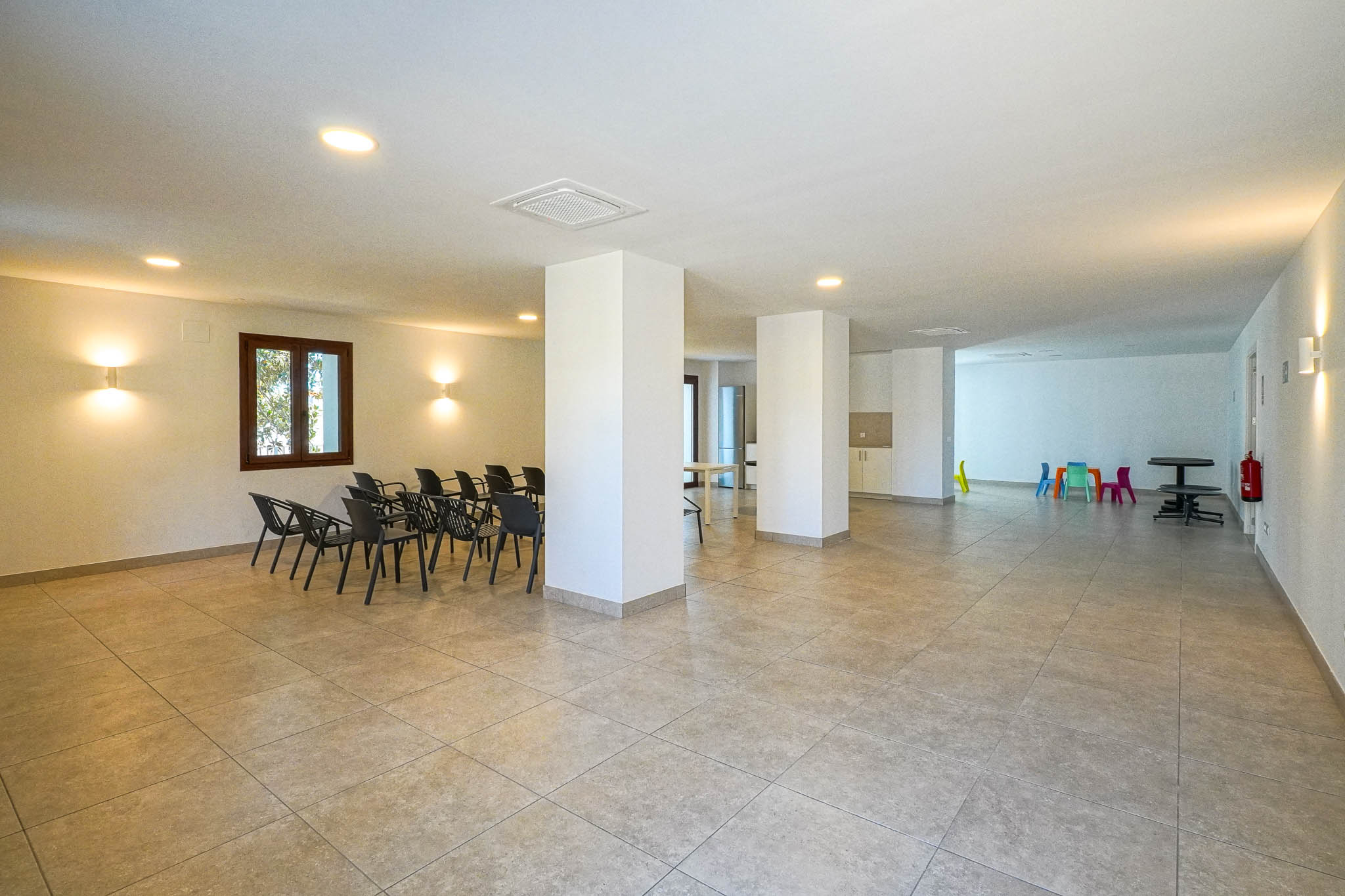 Spacious communal social center featuring tiled flooring, structural pillars, and recessed lighting. Includes a seating area for meetings and a colorful children's play corner.