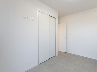 Bedroom featuring a spacious built-in wardrobe with white sliding doors and light grey tiled flooring. Modern electrical and data outlets are visible.
