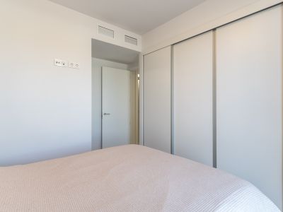Bedroom view featuring a spacious built-in wardrobe with white sliding doors. The wall includes modern electrical outlets and integrated ventilation grilles above the adjacent doorway.