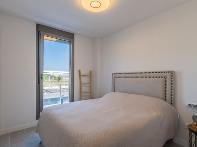 Bright bedroom featuring a bed with a studded fabric headboard and a built-in wardrobe. Large window offers outdoor access and natural light; grey tiled floor.