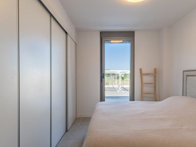 Bright bedroom featuring a built-in wardrobe with white sliding doors, tiled flooring, and direct access to the exterior through a glass door. Includes a bed with a studded headboard.