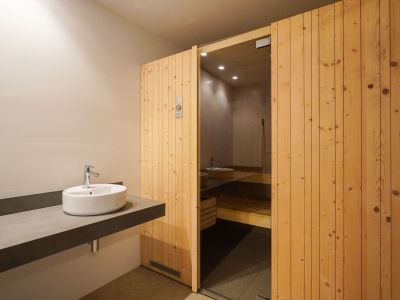 Changing area featuring a sleek floating vanity with a vessel sink and the inviting wooden-slatted sauna door with a glass panel, part of the communal social center.