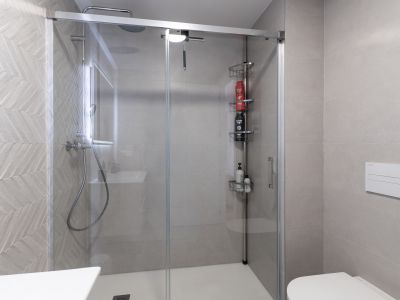 Contemporary bathroom featuring a glass shower enclosure and white tray. Light grey tiles with a distinct herringbone pattern adorn the shower wall, complemented by a rain shower and wall-mounted toilet.