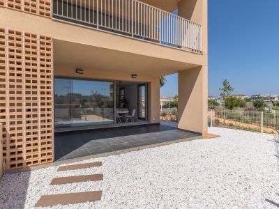 Covered ground-floor terrace with dark grey tiles, directly accessing a private white gravel garden. Large glass doors reveal a bright interior dining space, complemented by a modern decorative brick facade.