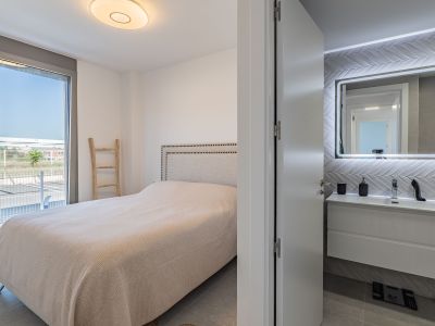 Main bedroom featuring a padded headboard bed and direct access to an outdoor terrace. An en-suite bathroom with a floating vanity and backlit mirror is visible.