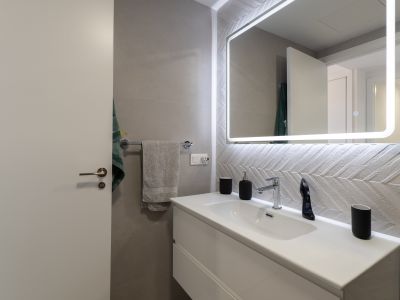 Modern bathroom featuring a white floating vanity, chrome faucet, and an illuminated mirror. Accentuated by textured chevron wall tiles.
