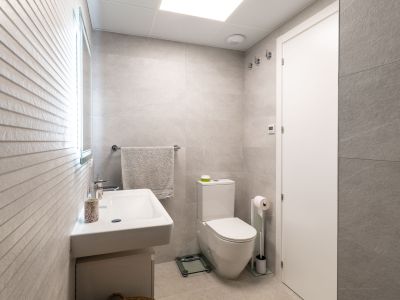 Modern bathroom featuring light grey large-format tiles, a wall-mounted sink, and a toilet. The illuminated mirror complements the textured accent wall.
