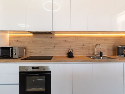 Modern kitchen featuring glossy white cabinetry, a wood-effect countertop and backsplash, and warm under-cabinet LED lighting. Includes integrated oven, induction hob, and microwave.