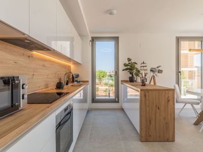 Modern open-plan kitchen featuring glossy white cabinetry, wood-effect countertops and backsplash, with integrated appliances and under-cabinet LED lighting. Offers direct access to the outdoor area.