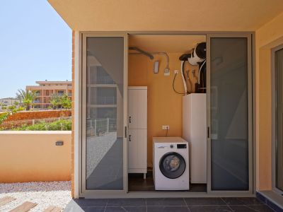 Outdoor utility room featuring a Bosch washing machine and aerothermal system, accessed from a tiled terrace with decorative pebbles and garden views.