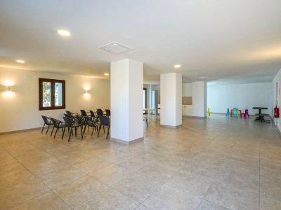 Spacious communal social center featuring tiled flooring, structural pillars, and recessed lighting. Includes a seating area for meetings and a colorful children's play corner.