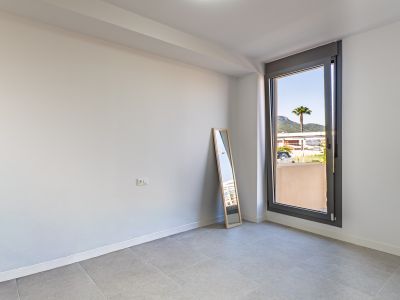 Unfurnished room featuring white walls and grey tiled flooring, ready for customization. Large window offers natural light and views of a palm tree and distant mountains.