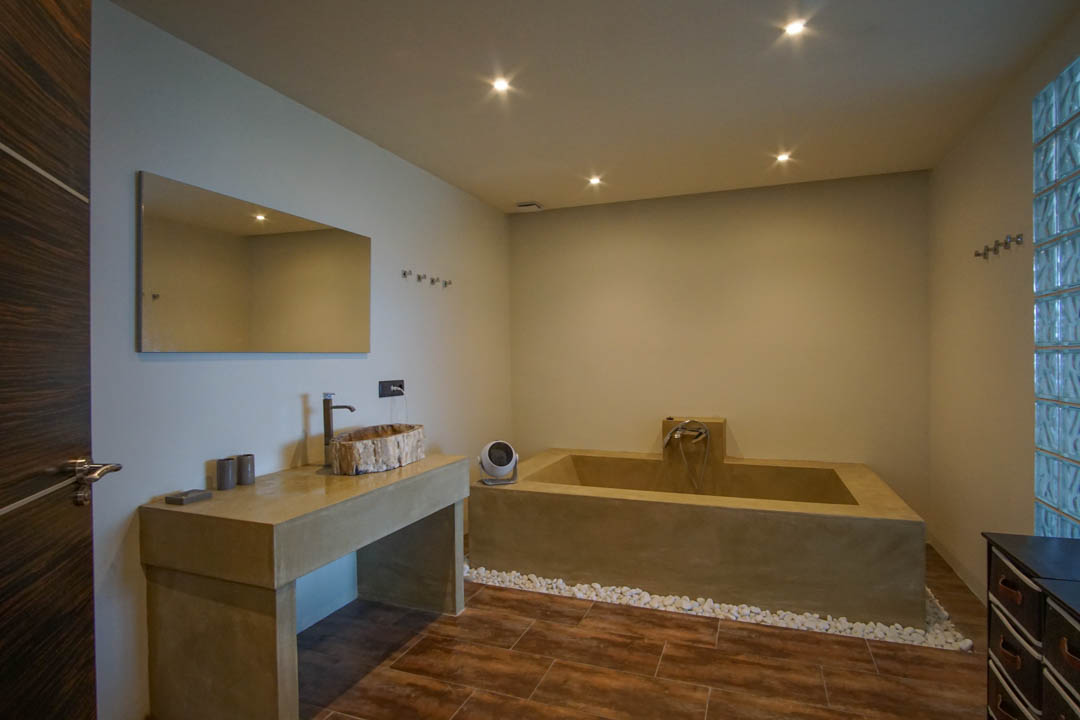 Modern bathroom featuring a unique wooden basin on a concrete-look vanity, a built-in tub, and a glass block wall.