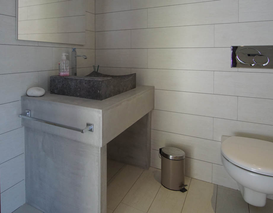 Modern guest toilet featuring a stone basin on a concrete-look vanity and light rectangular tiles. Wall-mounted toilet with chrome flush plate.