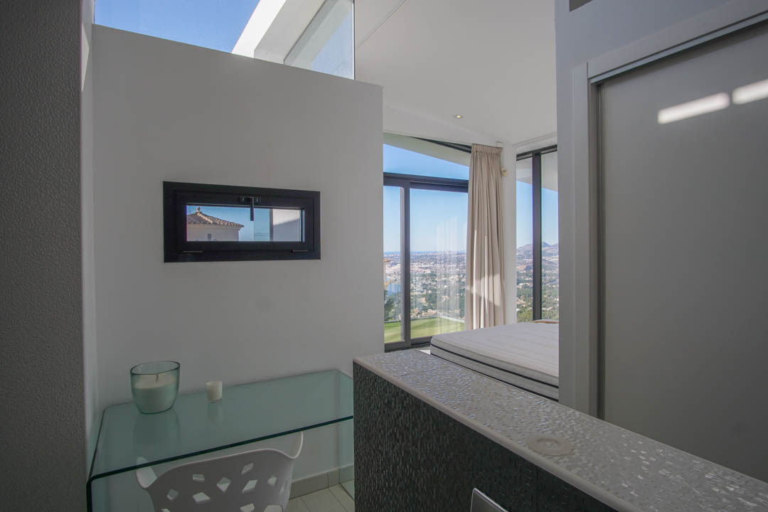 Study area with a glass desk and horizontal window, offering panoramic sea and city views from the adjacent bedroom.