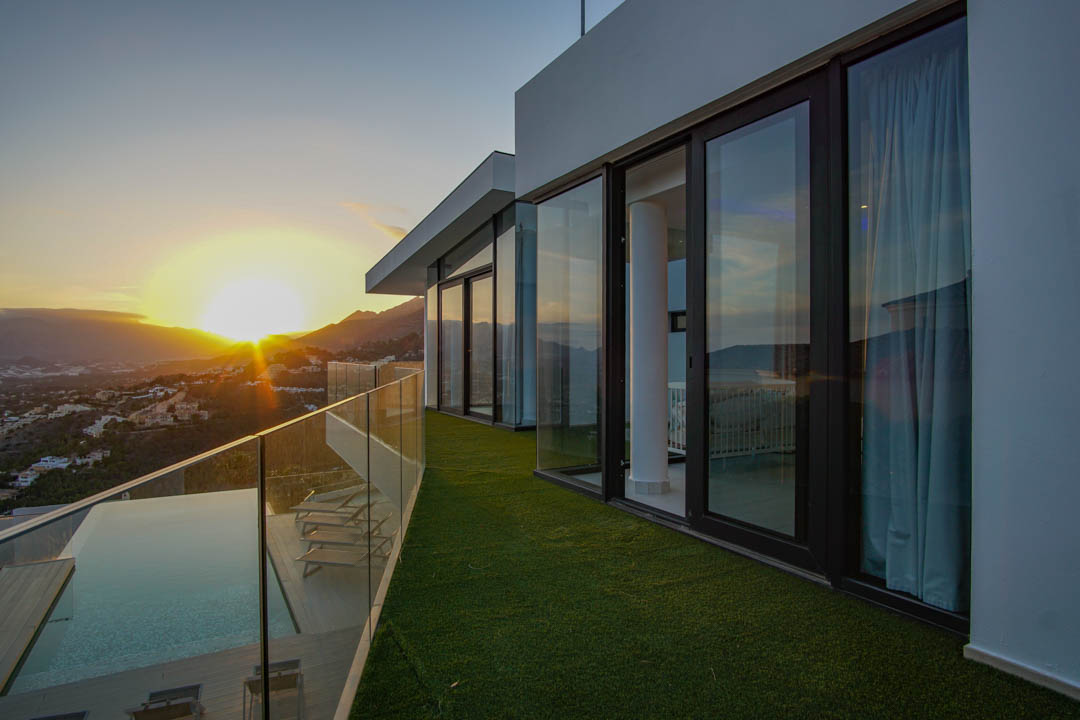 The expansive terrace features an infinity pool with wooden decking and glass balustrade, offering panoramic sunset views over the mountains and valley.