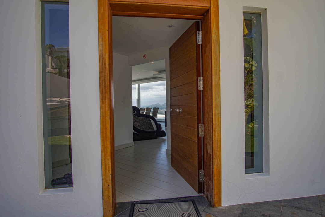 The open main entrance features a paneled wooden door and frame, flanked by vertical windows, offering a glimpse into the modern interior and distant mountain views.