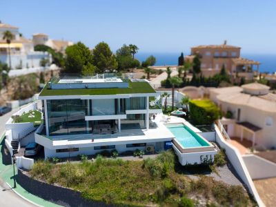 Aerial view of the modern white designer villa featuring a green roof, infinity pool, and separate jacuzzi, set against a sea view backdrop.