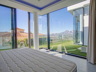 Bedroom featuring expansive corner glass walls, offering panoramic views of distant mountains, a valley, and neighboring rooftops. Includes a white structural pillar and direct access to an artificial lawn.