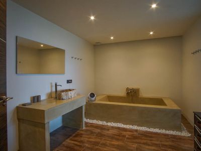Modern bathroom featuring a unique wooden basin on a concrete-look vanity, a built-in tub, and a glass block wall.