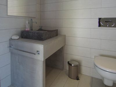 Modern guest toilet featuring a stone basin on a concrete-look vanity and light rectangular tiles. Wall-mounted toilet with chrome flush plate.