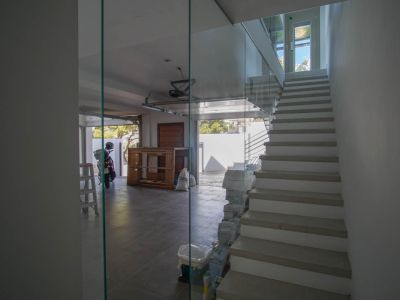 Modern interior staircase with glass balustrade and light-colored treads, adjacent to a tiled garage with an open door and natural light.