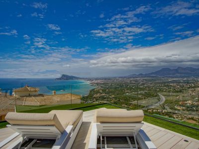 Rooftop terrace with two white sun loungers on a light wooden deck and artificial grass, offering panoramic views of the Mediterranean Sea, Altea coastline, and distant mountains.