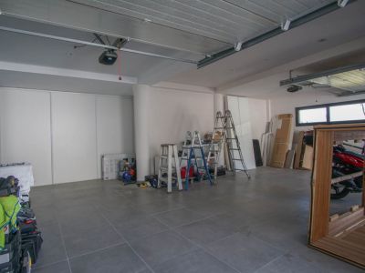 Spacious garage featuring grey tiled flooring and white walls. Equipped with two automatic door mechanisms, high horizontal windows, and white sliding storage doors.