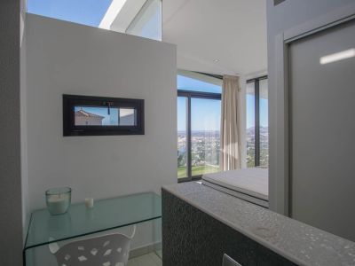 Study area with a glass desk and horizontal window, offering panoramic sea and city views from the adjacent bedroom.