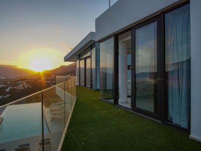 The expansive terrace features an infinity pool with wooden decking and glass balustrade, offering panoramic sunset views over the mountains and valley.
