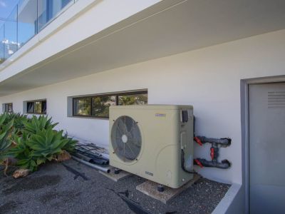The villa's exterior technical area features an AstralPool inverter heat pump, horizontal windows, and a utility door. Agave plants complement the modern white facade.