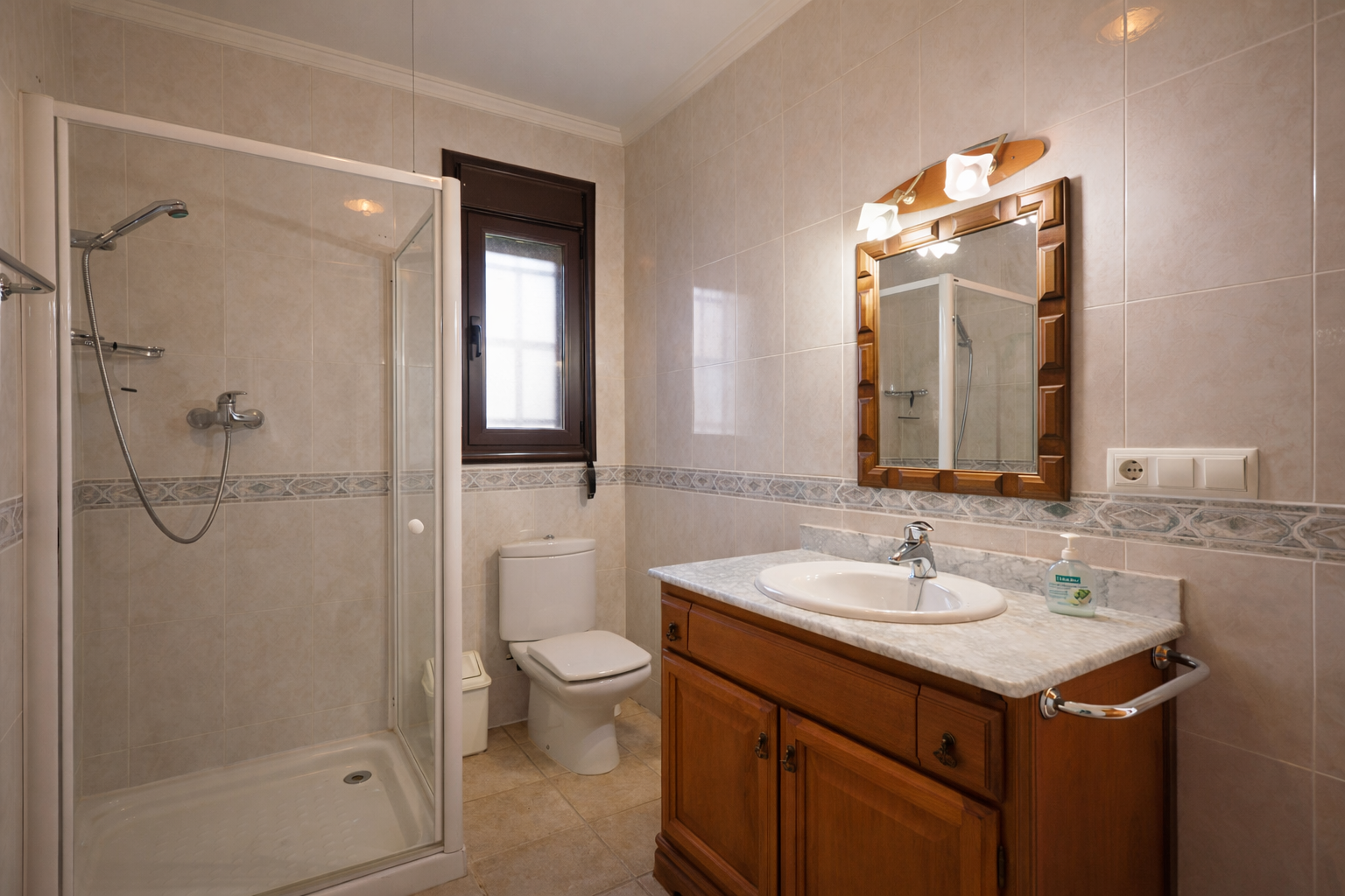 Bathroom featuring a walk-in shower with glass enclosure, toilet, and a wooden vanity with a marble countertop. Light-toned tiles adorn the walls and floor.