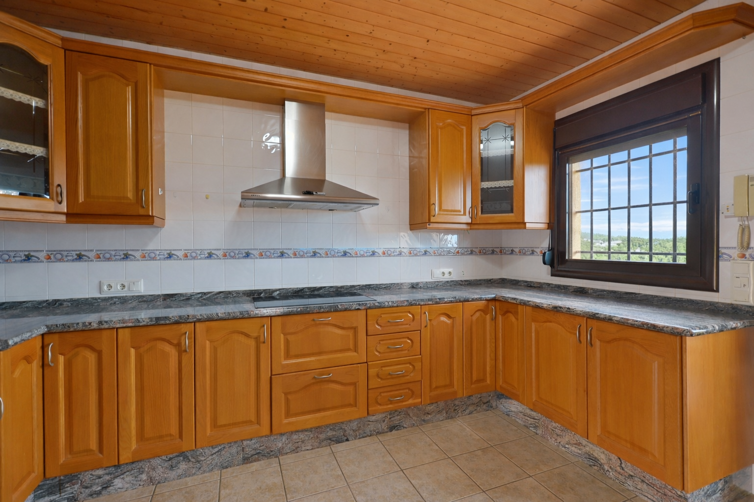 Equipped kitchen featuring wooden cabinetry, granite countertops, and a wooden plank ceiling. Window with security bars offers exterior views.