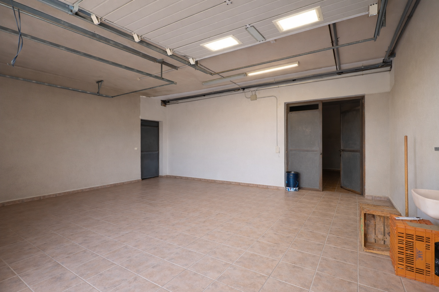 Spacious garage or utility room featuring light-tiled flooring, industrial ceiling lights, and multiple access points.