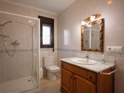 Bathroom featuring a walk-in shower with glass enclosure, toilet, and a wooden vanity with a marble countertop. Light-toned tiles adorn the walls and floor.