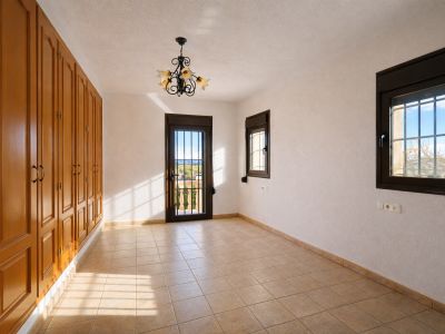 Bright room featuring extensive built-in wooden wardrobes, light tiled flooring, and textured white walls. Includes a balcony door with security bars, offering landscape views.