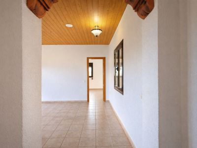 Interior hallway featuring light tiled flooring and textured white walls. Wooden plank ceiling with a central light and carved decorative arch details.