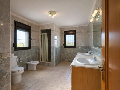 Spacious bathroom featuring a double vanity with marble countertop and wooden cabinet. Includes a walk-in shower, toilet, bidet, and two windows providing natural light.